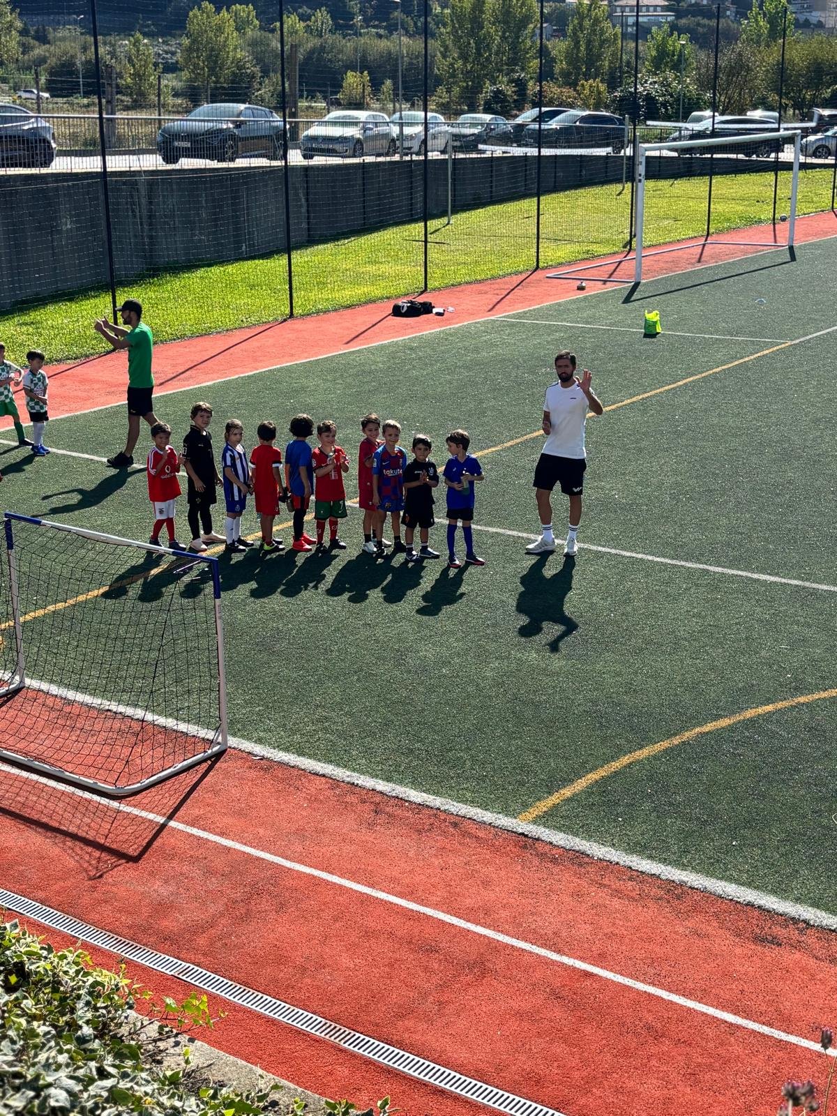 O treinador a falar com um grupo de crianças da Escola de Futebol, alinhadas em campo antes do jogo