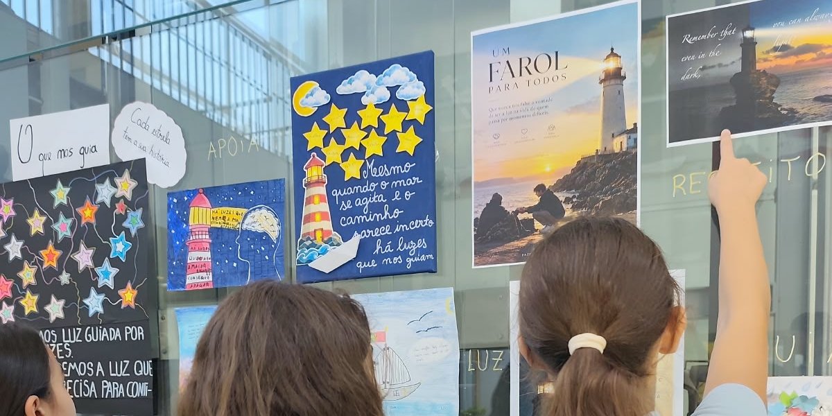 Alunas a observar os trabalhos sobre o tema do farol, expostos num vidro do colégio